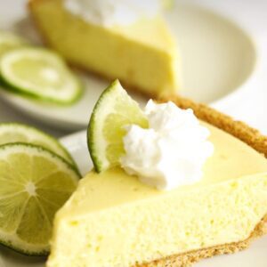 A slice of key lime pie with whipped cream and limes.