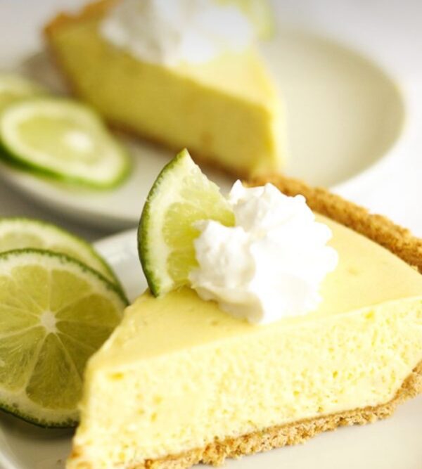 A slice of key lime pie with whipped cream and limes.