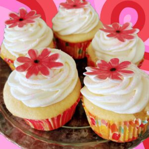 A plate of cupcakes with white frosting and red flowers.