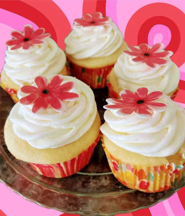 A plate of cupcakes with white frosting and red flowers.