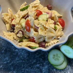 A bowl of pasta salad with cucumbers and tomatoes.